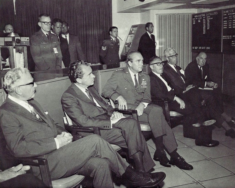 Original caption from 1970: DISTINGUISHED VISITORS - Richard M. Nixon is September 1969 became the first U.S. President to visit the underground command post of the North American Air Defense Command. He is shown here in NORAD’s Space Defense Center being briefed by General Seth J. McKee, commander in chief of NORAD. Left to right are: Gordon Allott, U.S. Senator from Colorado; President Nixon; General McKee; Dr. Henry A. Kissinger, Presidential assistant; Peter H. Dominick, U.S. Senator from Colorado; and John N. Mitchell, U.S. Attorney General. (Photo scanned by Memory Hole 2 from the book NORAD Command Post: The City Inside Cheyenne Mountain by Henry W. Hough)